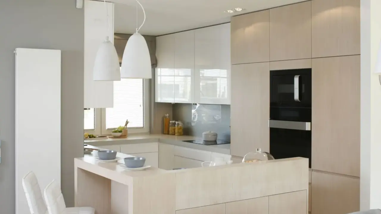 Jasne kuchnie inspiracje: nowoczesna zabudowa, wyspa z hokerami i eleganckie oświetlenie tworzą przytulną atmosferę.