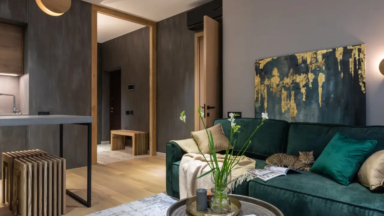 Elegancki salon w butelkowej zieleni i drewnie. Kot odpoczywa na kanapie, a w wazonie stoją świeże kwiaty.