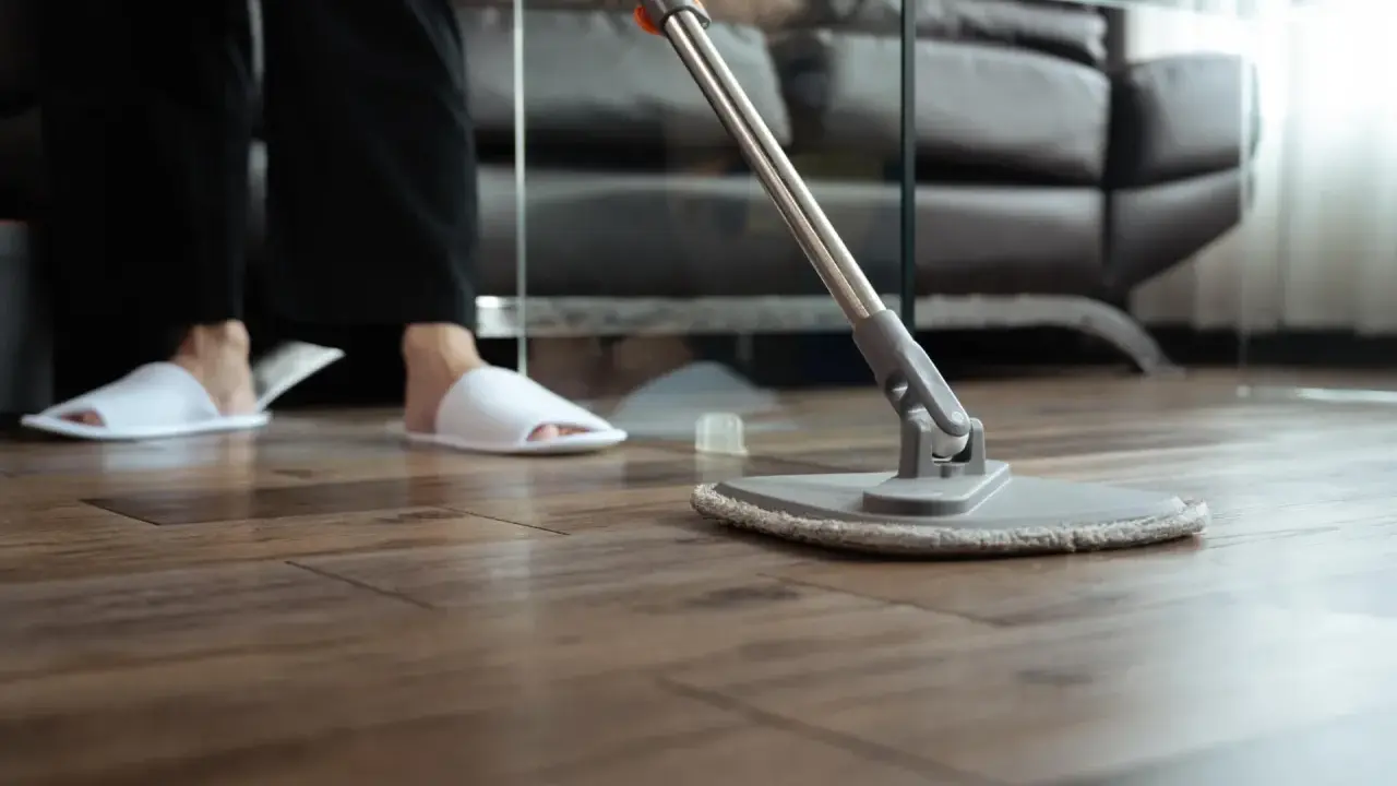 Osoba w kapciach czyści drewniany parkiet mopem. Proste sposoby, jak odnowić parkiet domowym sposobem, by znów lśnił.