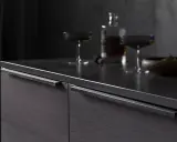 Elegancki front z uchwytem frezowanym, ciemne drewno, kieliszki i butelka z alkoholem na blacie.