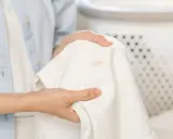 Dłonie trzymają białą tkaninę z plamami, zastanawiając się, czym zmyć wosk.