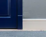 Granatowe drzwi i biała listwa przypodłogowa. Zastanawiasz się, gdzie zamontować odbojnik do drzwi? Tutaj widać, że można go zamontować przy framudze.