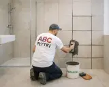 Fachowiec z koszulką "ABC PŁYTKI" fuguje ściany w łazience. Pokazuje, jak zmatowić płytki.