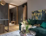 Elegancki salon w butelkowej zieleni i drewnie. Kot odpoczywa na kanapie, a w wazonie stoją świeże kwiaty.