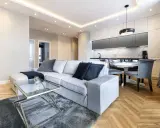 Nowoczesny salon z szarą sofą i szklanym stolikiem. Inspiracja, jak pomalować salon nowocześnie, z wykorzystaniem jasnych ścian i subtelnych dodatków.