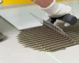 Równomierne rozprowadzanie kleju pod płytki za pomocą kielni. Precyzyjne linie kleju i zielona linia lasera zapewniają idealne ułożenie.