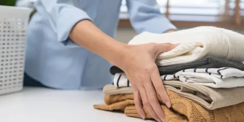 Dłoń układa stos ubrań. Dowiedz się, jak usunąć zapach perfum z ubrania, aby cieszyć się świeżością.