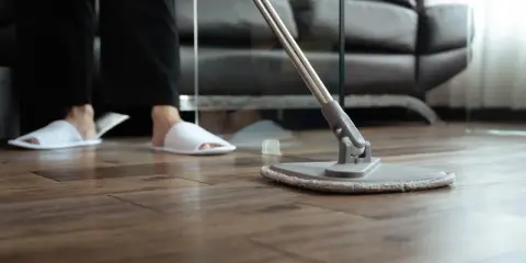Osoba w kapciach czyści drewniany parkiet mopem. Proste sposoby, jak odnowić parkiet domowym sposobem, by znów lśnił.