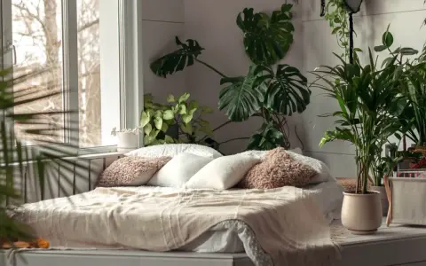 Przytulna sypialnia w stylu urban jungle. Duże liście monstery i palmy tworzą zieloną oazę wokół łóżka.