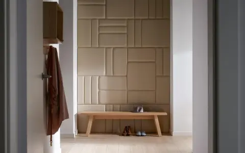 Nowoczesny pomysł na ścianę w korytarzu: tapicerowane panele w geometryczne wzory, drewniana ławka, płaszcz i buty.