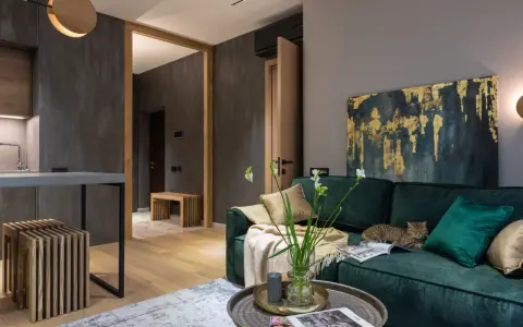 Elegancki salon w butelkowej zieleni i drewnie. Kot odpoczywa na kanapie, a w wazonie stoją świeże kwiaty.