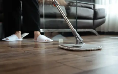 Osoba w kapciach czyści drewniany parkiet mopem. Proste sposoby, jak odnowić parkiet domowym sposobem, by znów lśnił.