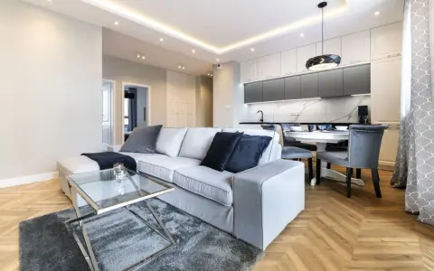 Nowoczesny salon z szarą sofą i szklanym stolikiem. Inspiracja, jak pomalować salon nowocześnie, z wykorzystaniem jasnych ścian i subtelnych dodatków.