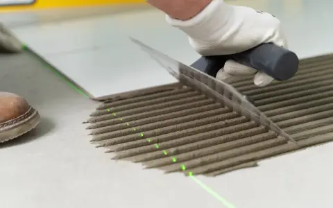 Równomierne rozprowadzanie kleju pod płytki za pomocą kielni. Precyzyjne linie kleju i zielona linia lasera zapewniają idealne ułożenie.