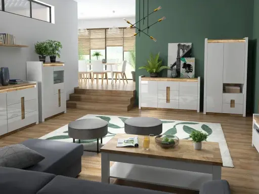 Nowoczesny salon z szarą kanapą, drewnianym stolikiem i komodami. Jedna ściana innego koloru, zielona, dodaje głębi.