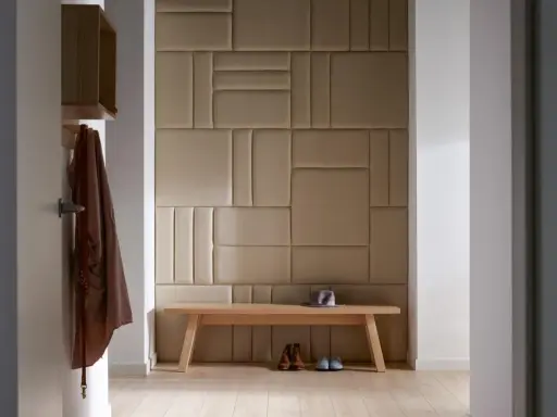 Nowoczesny pomysł na ścianę w korytarzu: tapicerowane panele w geometryczne wzory, drewniana ławka, płaszcz i buty.