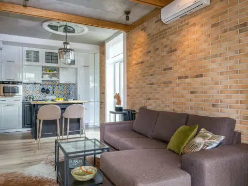 Nowoczesny styl rustykalny w salonie z ceglaną ścianą, wygodną kanapą i aneksem kuchennym.
