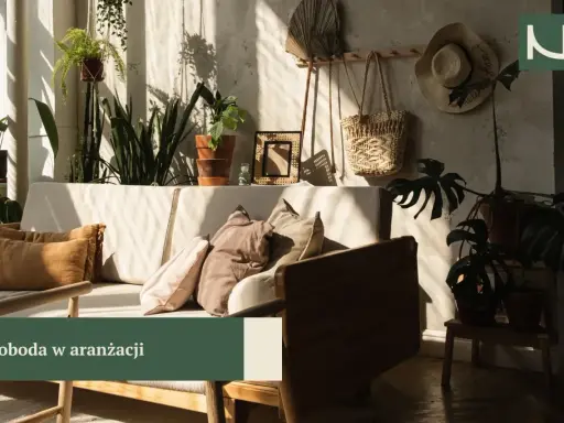 Przytulny salon boho z dużą ilością roślin, plecionym koszem i słomkowym kapeluszem na ścianie. Miękkie poduszki na kanapie zapraszają do relaksu.