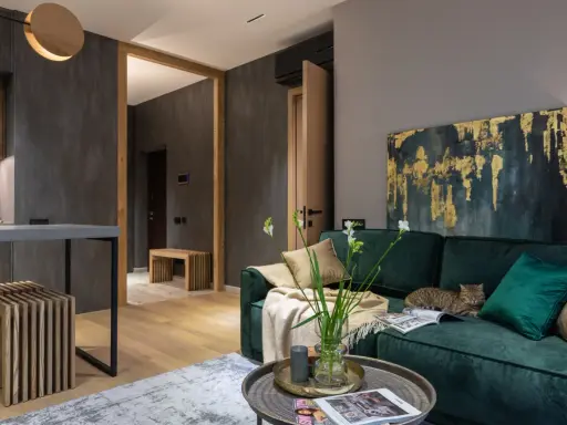 Elegancki salon w butelkowej zieleni i drewnie. Kot odpoczywa na kanapie, a w wazonie stoją świeże kwiaty.