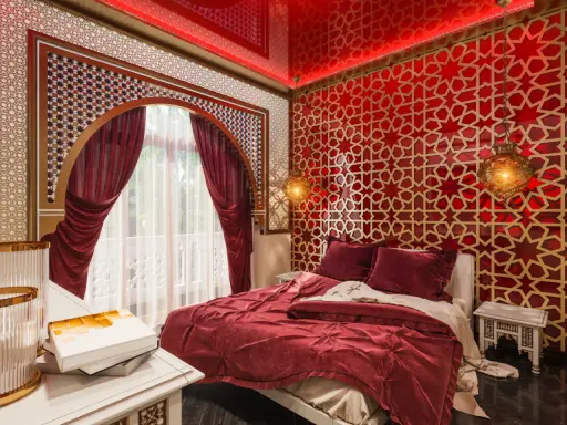 Luksusowa sypialnia w stylu marokańskim. Czerwone ściany z geometrycznymi wzorami, bogato zdobione łóżko i orientalne lampy tworzą magiczną atmosferę.
