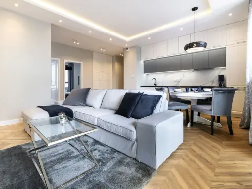 Nowoczesny salon z szarą sofą i szklanym stolikiem. Inspiracja, jak pomalować salon nowocześnie, z wykorzystaniem jasnych ścian i subtelnych dodatków.
