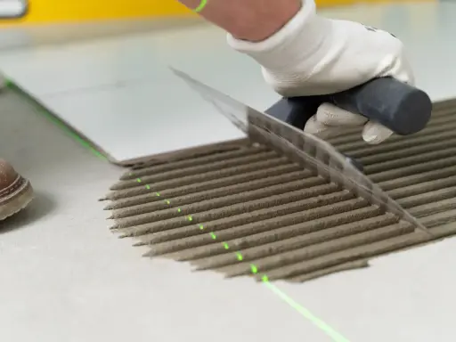 Równomierne rozprowadzanie kleju pod płytki za pomocą kielni. Precyzyjne linie kleju i zielona linia lasera zapewniają idealne ułożenie.