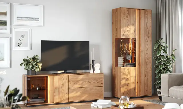 Nowoczesny salon z drewnianą komodą, na której stoi telewizor. Obok komody wysoka witryna z przeszkloną częścią.