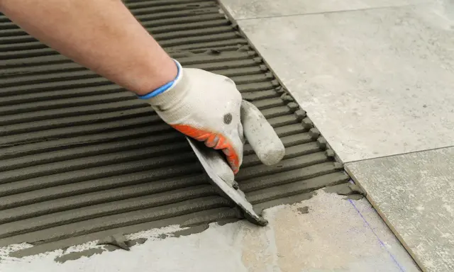 Ręka w rękawicy rozprowadza klej kielnią, przygotowując podłoże do tego, jak układać płytki na schodach zewnętrznych.