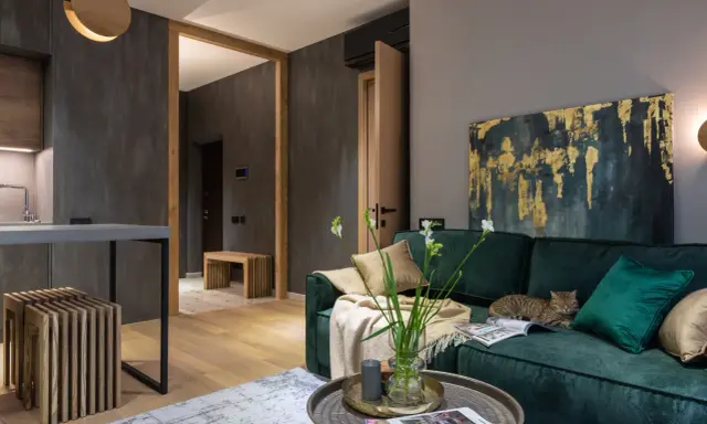 Elegancki salon w butelkowej zieleni i drewnie. Kot odpoczywa na kanapie, a w wazonie stoją świeże kwiaty.