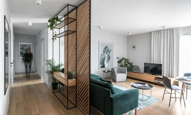 Drewniana struktura na ścianę w korytarzu z półkami i roślinami, oddzielająca przestrzeń od salonu.