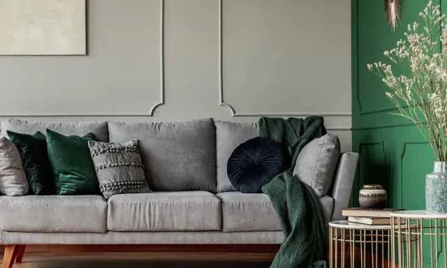Szara kanapa z zielonymi poduszkami i kocem. Pokazuje, jaki kolor pasuje do szarego w salonie, tworząc elegancką aranżację.