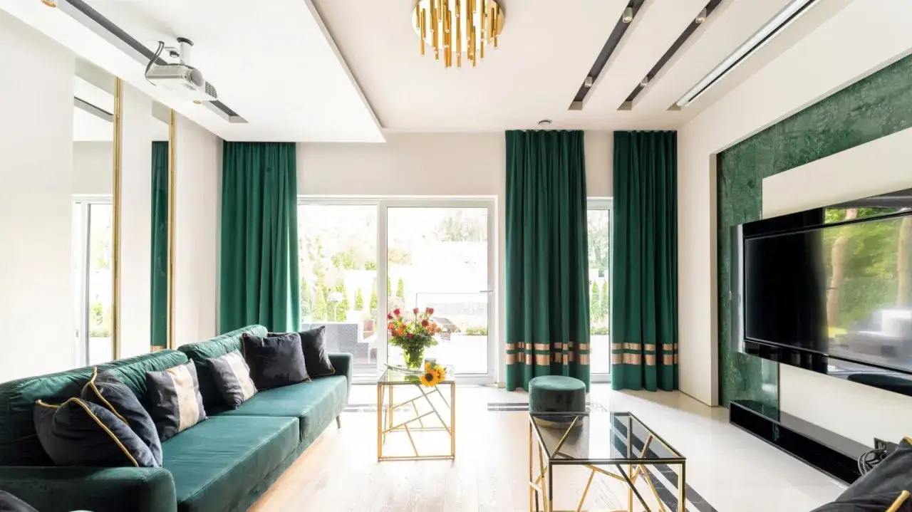 Elegancki salon z zieloną kanapą i zasłoną z jednej strony okna. Złote dodatki i marmurowa ściana dodają luksusu.