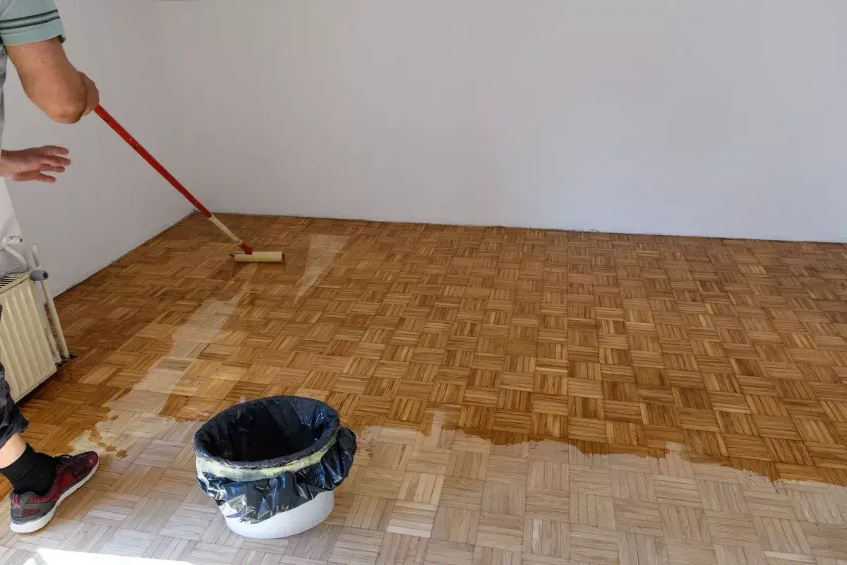 Odnawianie parkietu domowym sposobem: aplikacja lakieru wałkiem na drewnianą podłogę.