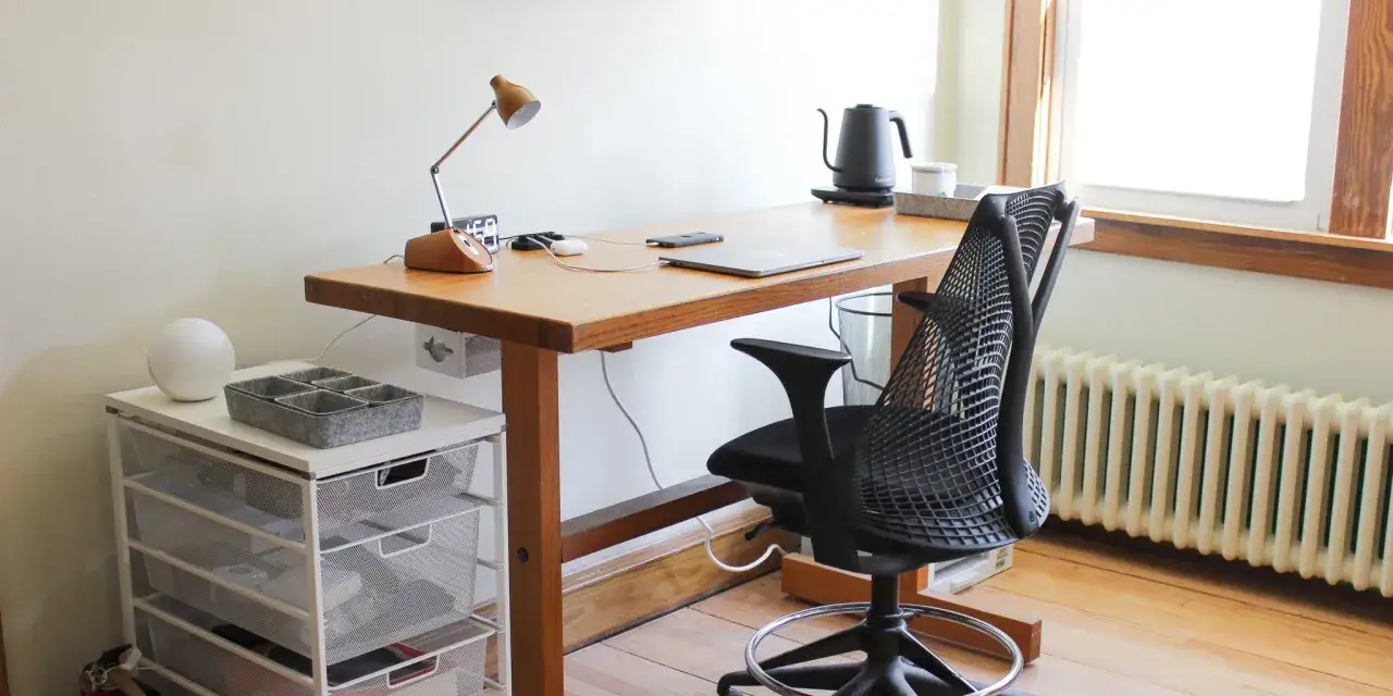 Organizacja biurka inspiracje: drewniany blat, czarne krzesło, lampka, laptop i organizer na drobiazgi.