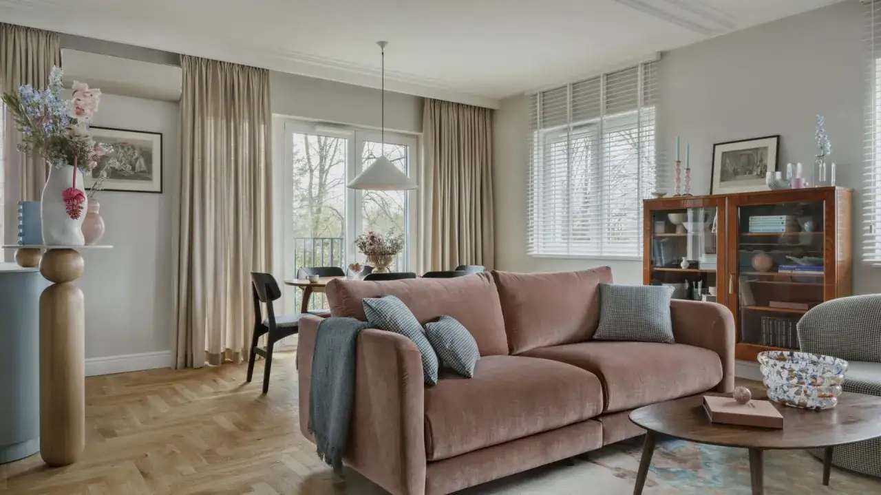 Przytulny salon z r&oacute;żową kanapą na środku. W tle widać st&oacute;ł z krzesłami i przeszkloną witrynę.