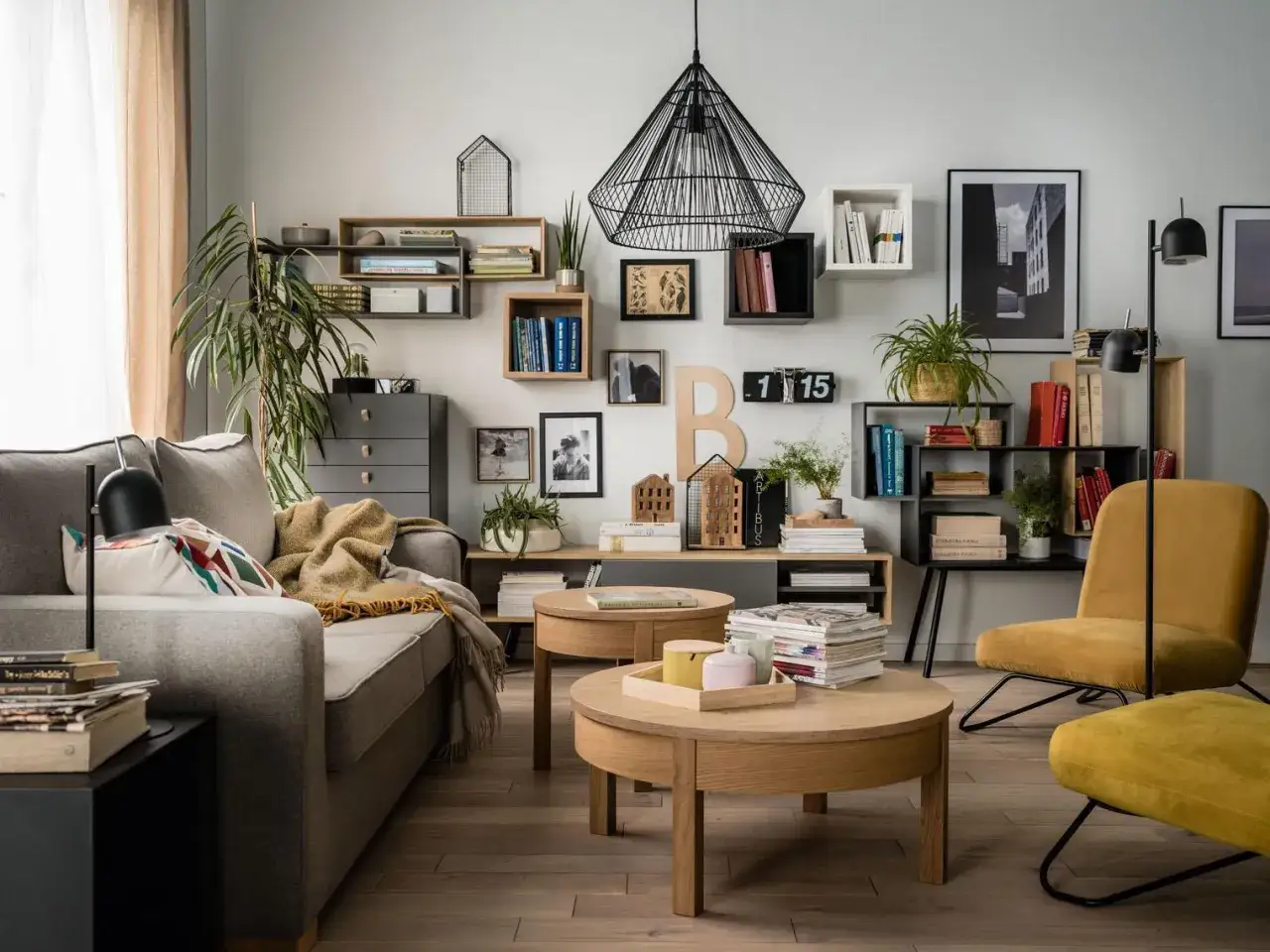 Inspiracja, jak rozmieścić p&oacute;łki na ścianie: nowoczesny salon z szarą kanapą, drewnianymi stolikami i ż&oacute;łtym fotelem.