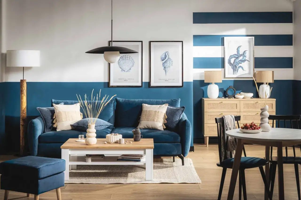 Przytulny salon w stylu marynistycznym. Granatowa sofa, morskie dekoracje i biało-niebieskie pasy na ścianie tworzą nadmorski klimat.
